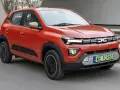 Pomarańczowy Dacia Spring, najtańsze auto elektryczne, jedzie po drodze.