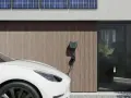 Białe auto elektryczne (BEV) podłączone do ładowarki przy nowoczesnym domu z panelami słonecznymi.