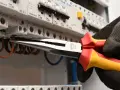 Elektryk w rękawicy wymienia instalację elektryczną, używając kombinerki do przewodów w skrzynce z bezpiecznikami.