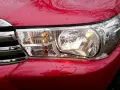 Czerwony samochód z błyszczącym chromowanym grillem i włączonym reflektorem. Widać odbłyśnik światła.