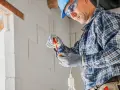 Elektryk w kasku i okularach montuje oprawkę żarówki. Sprawdź nasze usługi elektryczne cennik.