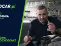 Mężczyzna pokazuje, jak wymienić żarówkę w aucie. W tle warsztat z narzędziami.