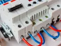 Montaż ogranicznika przepięć. Widoczne białe moduły elektryczne z czerwonymi i niebieskimi przewodami, gotowe do podłączenia.