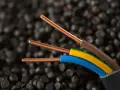Trzy miedziane żyły kabla elektrycznego, w izolacjach brązowej, żółto-zielonej i niebieskiej, na tle granulatów tworzywa sztucznego. Idealne do instalacji IP20.