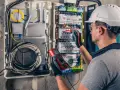 Elektryk z multimetrem sprawdza instalację elektryczną, dbając o kompensację mocy biernej.