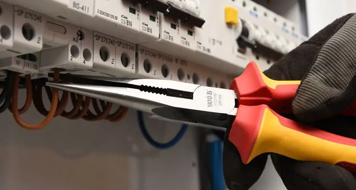 Elektryk w rękawicy wymienia instalację elektryczną, używając kombinerki do przewodów w skrzynce z bezpiecznikami.