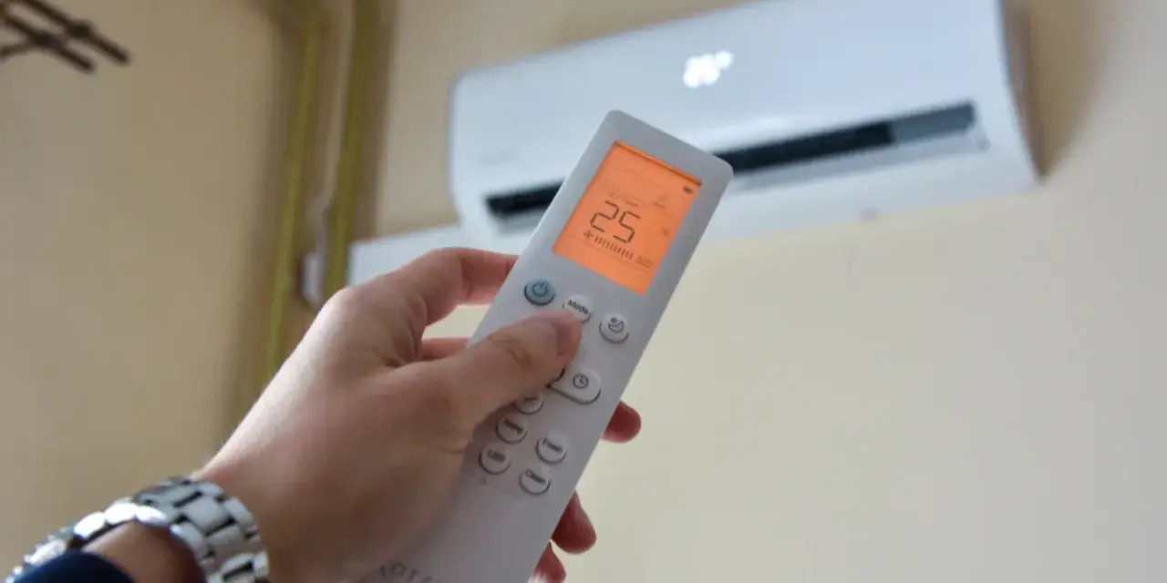 Dłoń trzymająca pilot do klimatyzacji, ustawiona na 25°C. Kontroluj komfort i miesięczny koszt klimatyzacji.