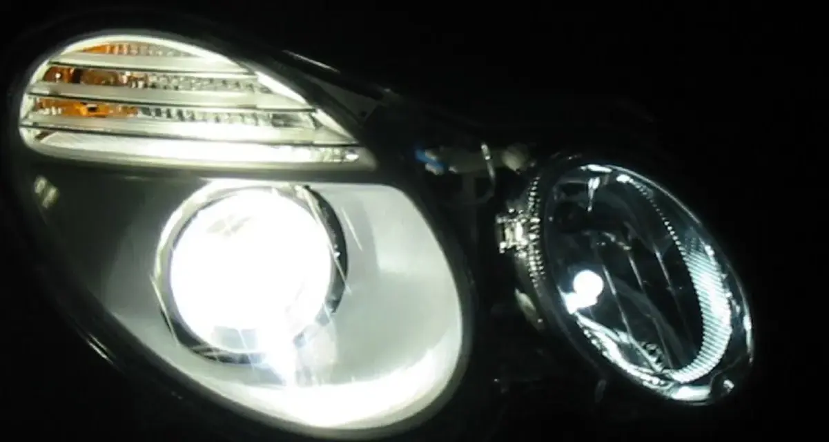 Jasny ksenon rozświetla reflektor, ukazując jego nowoczesny design i pomarańczowe kierunkowskazy.
