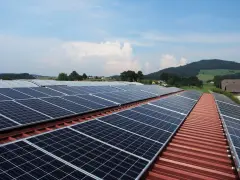 Duże panele PV na dachu budynku gospodarczego, otoczonego zielonymi wzgórzami.