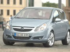 Jasnoniebieski Opel Corsa D z włączonymi żarówkami z przodu, zaparkowany na bruku.