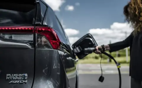 Kobieta podłącza ładowarkę do hybrydowego SUV-a. Zastanawiasz się, ile kosztuje ładowanie elektryka?