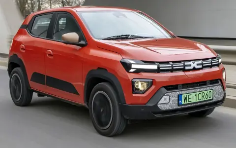 Pomarańczowy Dacia Spring, najtańsze auto elektryczne, jedzie po drodze.
