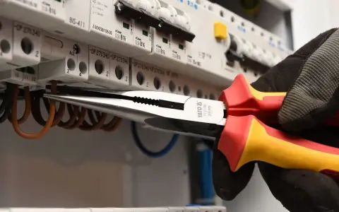 Elektryk w rękawicy wymienia instalację elektryczną, używając kombinerki do przewodów w skrzynce z bezpiecznikami.