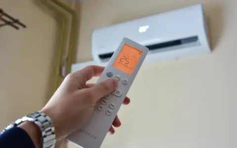 Dłoń trzymająca pilot do klimatyzacji, ustawiona na 25°C. Kontroluj komfort i miesięczny koszt klimatyzacji.
