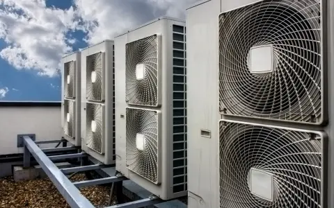 Rząd jednostek klimatyzacyjnych na dachu pod błękitnym niebem z chmurami.