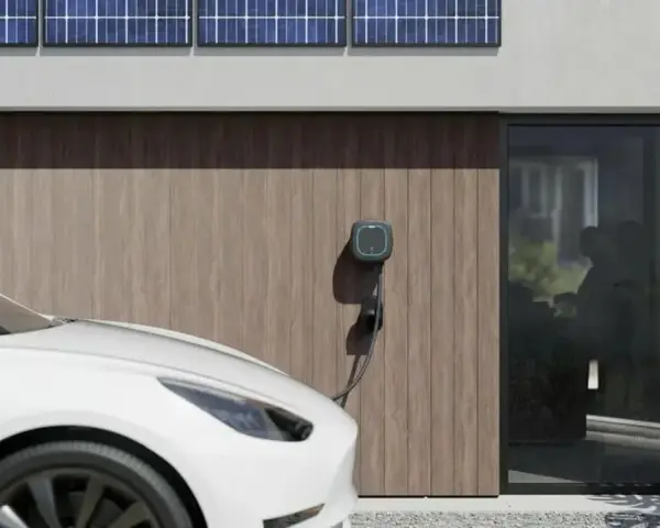Białe auto elektryczne (BEV) podłączone do ładowarki przy nowoczesnym domu z panelami słonecznymi.