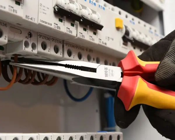 Elektryk w rękawicy wymienia instalację elektryczną, używając kombinerki do przewodów w skrzynce z bezpiecznikami.