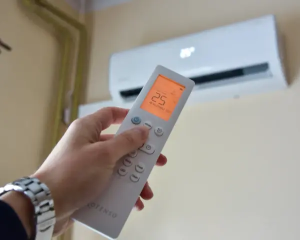 Dłoń trzymająca pilot do klimatyzacji, ustawiona na 25°C. Kontroluj komfort i miesięczny koszt klimatyzacji.