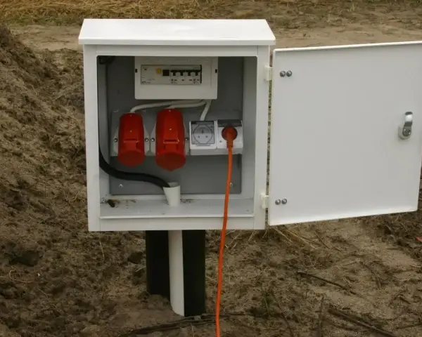 Skrzynka elektryczna na działce bez domu, gotowa do podłączenia prądu. Widoczne gniazda i zabezpieczenia.