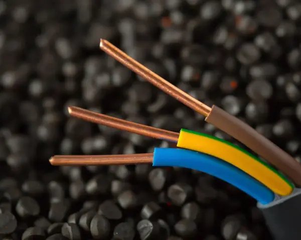 Trzy miedziane żyły kabla elektrycznego, w izolacjach brązowej, żółto-zielonej i niebieskiej, na tle granulatów tworzywa sztucznego. Idealne do instalacji IP20.