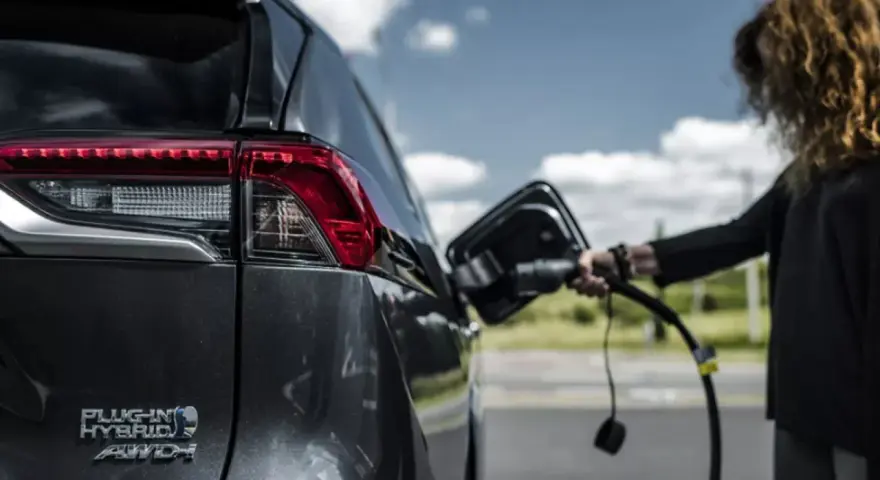 Kobieta podłącza ładowarkę do hybrydowego SUV-a. Zastanawiasz się, ile kosztuje ładowanie elektryka?