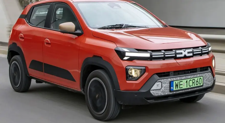 Pomarańczowy Dacia Spring, najtańsze auto elektryczne, jedzie po drodze.