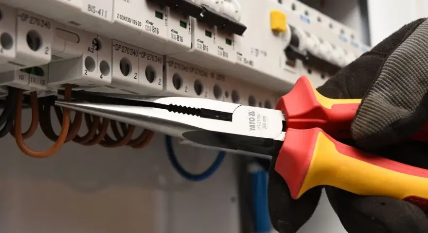 Elektryk w rękawicy wymienia instalację elektryczną, używając kombinerki do przewodów w skrzynce z bezpiecznikami.