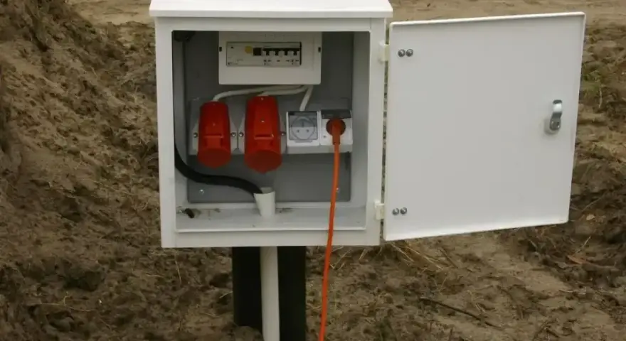 Skrzynka elektryczna z zabezpieczeniami i gniazdami, gotowa do tauron przyłączenie prądu do działki. Pomarańczowy kabel wpięty do gniazda.