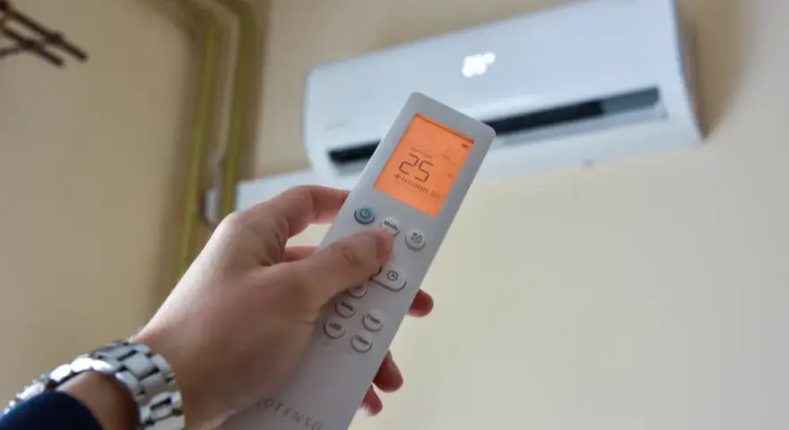 Dłoń trzymająca pilot do klimatyzacji, ustawiona na 25°C. Kontroluj komfort i miesięczny koszt klimatyzacji.