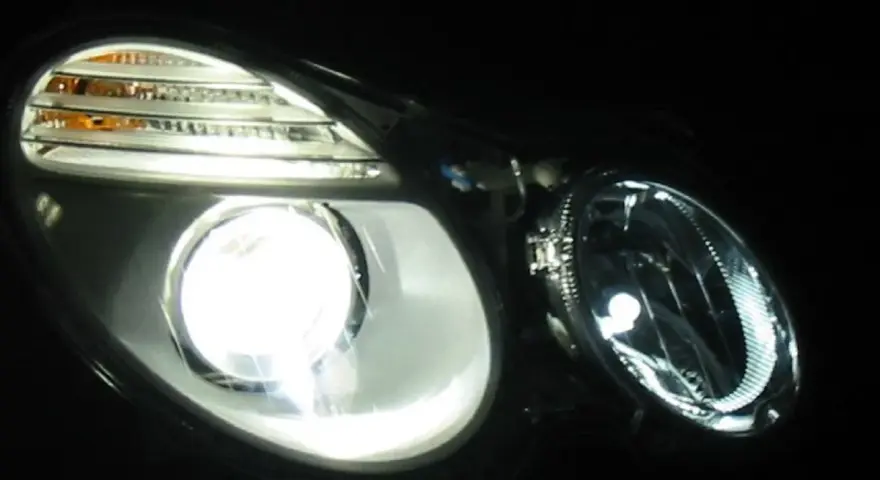 Jasny ksenon rozświetla reflektor, ukazując jego nowoczesny design i pomarańczowe kierunkowskazy.