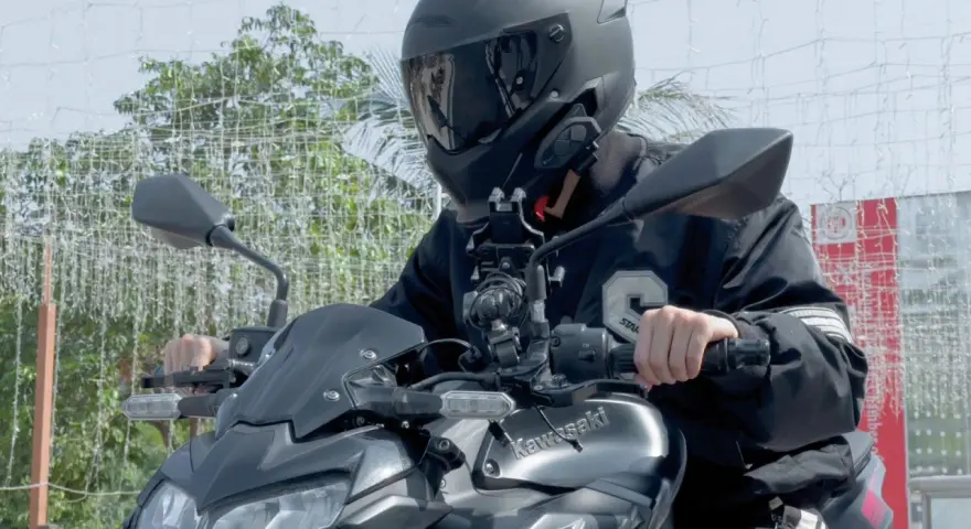 Motocyklista w kasku siedzi na motocyklu Kawasaki, z zamontowanym interkomem na kasku.