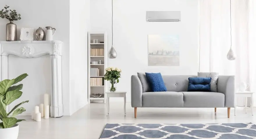 Nowoczesny salon z klimatyzacją w trybie funkcja dry, szara kanapa, kominek, regał i dywan.