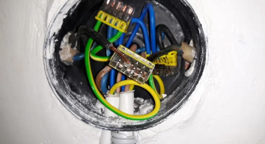 Wnętrze puszki elektrycznej z przewodami: niebieskim, zielono-żółtym i brązowym, połączonymi złączkami. Trwa zerowanie gniazdka.