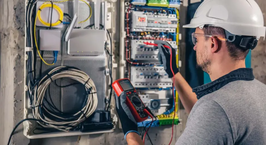 Elektryk z multimetrem sprawdza instalację elektryczną, dbając o kompensację mocy biernej.